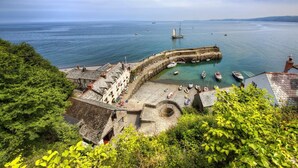 Un pueblo costero con un muelle de piedra histórico, barcos amarrados y abundante vegetación.