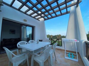 A patio with a table and chairs, a grill, and a view of the landscape.