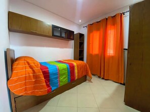 A room with a bed, a wardrobe, a shelf unit, and orange curtains. - Serene 2-bedroom apartment in Cabo Negro with view of golf course (Cabo Negro)