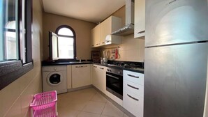 A compact kitchen with a washing machine, a stove, and a refrigerator. - Serene 2-bedroom apartment in Cabo Negro with view of golf course (Cabo Negro)