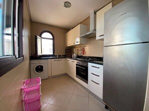 A compact kitchen with a washing machine, a stove, and a refrigerator. - Serene 2-bedroom apartment in Cabo Negro with view of golf course (Cabo Negro)