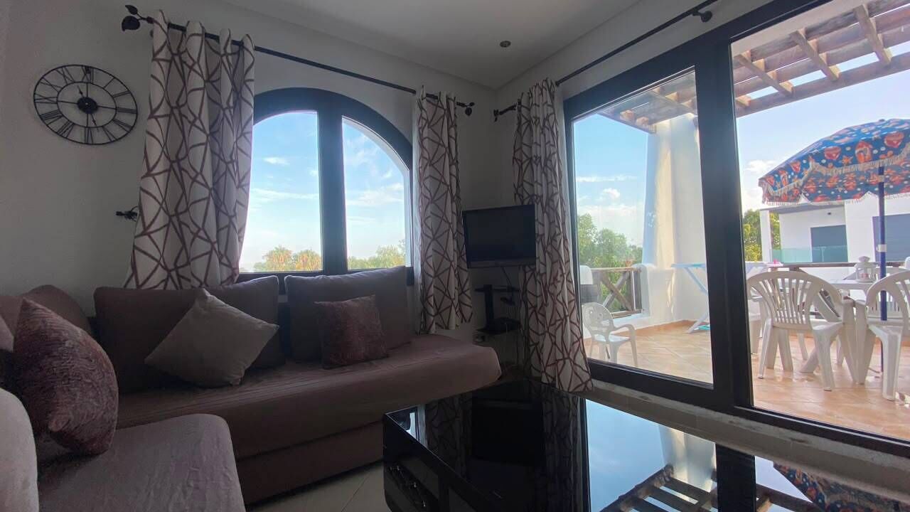 Una sala de estar con sofá, televisor y ventanas amplias.