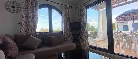 Una sala de estar con sofá, televisor y ventanas amplias.