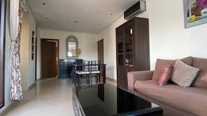 A living room with a sofa, a glass coffee table, a dining area with chairs, and a cabinet.