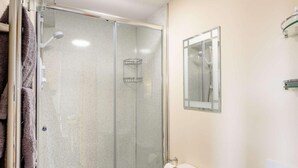 Et badeværelse med en glasvæg omkring brusenichen, toilet og et spejl.
