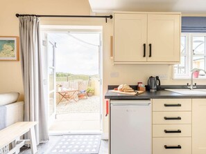 A compact kitchen with a refrigerator, a sink, and a dining area with a table and chairs. - 1 Bed in Umberleigh (oc-81426) (High Bickington)