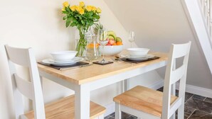 Et spisebord dækket med hvide stole, en vase med gule blomster, en skål med frugt og vinglas.