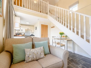 A living room with a beige sofa, two pillows, a staircase with white balusters, and a kitchen in the background. - 1 Bed in Umberleigh (oc-81426) (High Bickington)