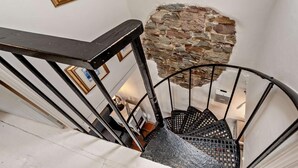 Una escalera de caracol con pared de piedra, barandilla de metal negro y un cuadro enmarcado en la pared.