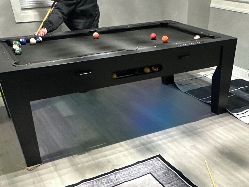A pool table with balls, a cue stick, and a person playing.