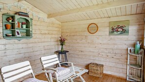 A cozy room with wooden walls, a green shelf with books and flowers, two white chairs, a small table with a vase, and a wicker basket. - 1 Bed in Wootton (oc-ic159) (Wootton Bridge)