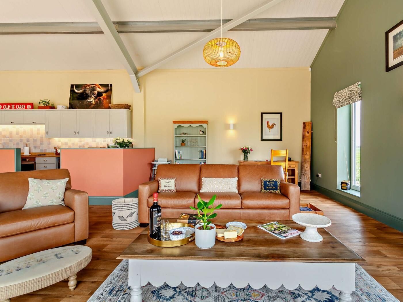 A living room with a sofa set, a coffee table with food and drinks, a bookshelf, and a kitchen area in the background.