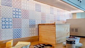 Comptador de cuina amb diverses formatges, una caixa de pa, un botic de conserves i una paret decorativa amb rajoles estampades.