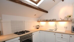 Une cuisine avec des armoires blanches, une cuisinière, un évier et une poutre en bois au plafond.