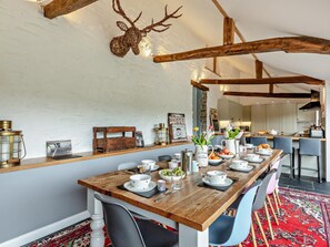 A dining area with a wooden table set for four, surrounded by chairs, and a red patterned rug on the floor. - 5 Bed in Dulverton (oc-41133) (Brushford)