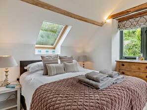 A bedroom with a sloped ceiling, a skylight, a bed with a brown quilt, two bedside tables with lamps, and a dresser with a window view. - 5 Bed in Dulverton (oc-41133) (Brushford)