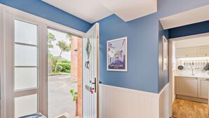 Un couloir avec une porte donnant sur l’extérieur, une affiche accrochée au mur et un coin cuisine avec des placards et des ustensiles.