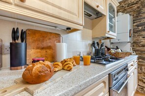 A kitchen with a granite countertop, a loaf of bread, croissants, and glasses of orange juice. - 1 Bed in Bideford (oc-63059) (Northam)