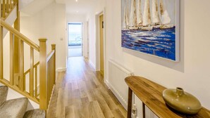 Ein Flur mit Holzboden, einer Treppe mit Holzwandleisten und einem Gemälde von Segelbooten an der Wand.