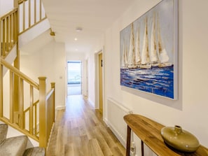 Ein Flur mit Holzboden, einer Treppe mit Holzwandleisten und einem Gemälde von Segelbooten an der Wand.