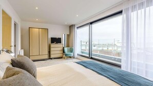 Ein modernes Hotelzimmer mit einem großen Bett, einem Kleiderschrank, einem Fernseher, einem Sessel und einem Balkon mit Blick.