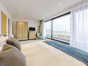 Ein modernes Hotelzimmer mit einem großen Bett, einem Kleiderschrank, einem Fernseher, einem Sessel und einem Balkon mit Blick.