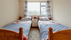 Een slaapkamer met twee éénpersoonsbedden, een nachtkastje met een lamp, een raam met gordijnen en uitzicht op buiten.