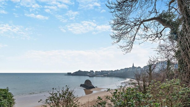 Een kustgezicht met een strand, rotsachtige landtongen en een verafgelegen stadsbeeld.