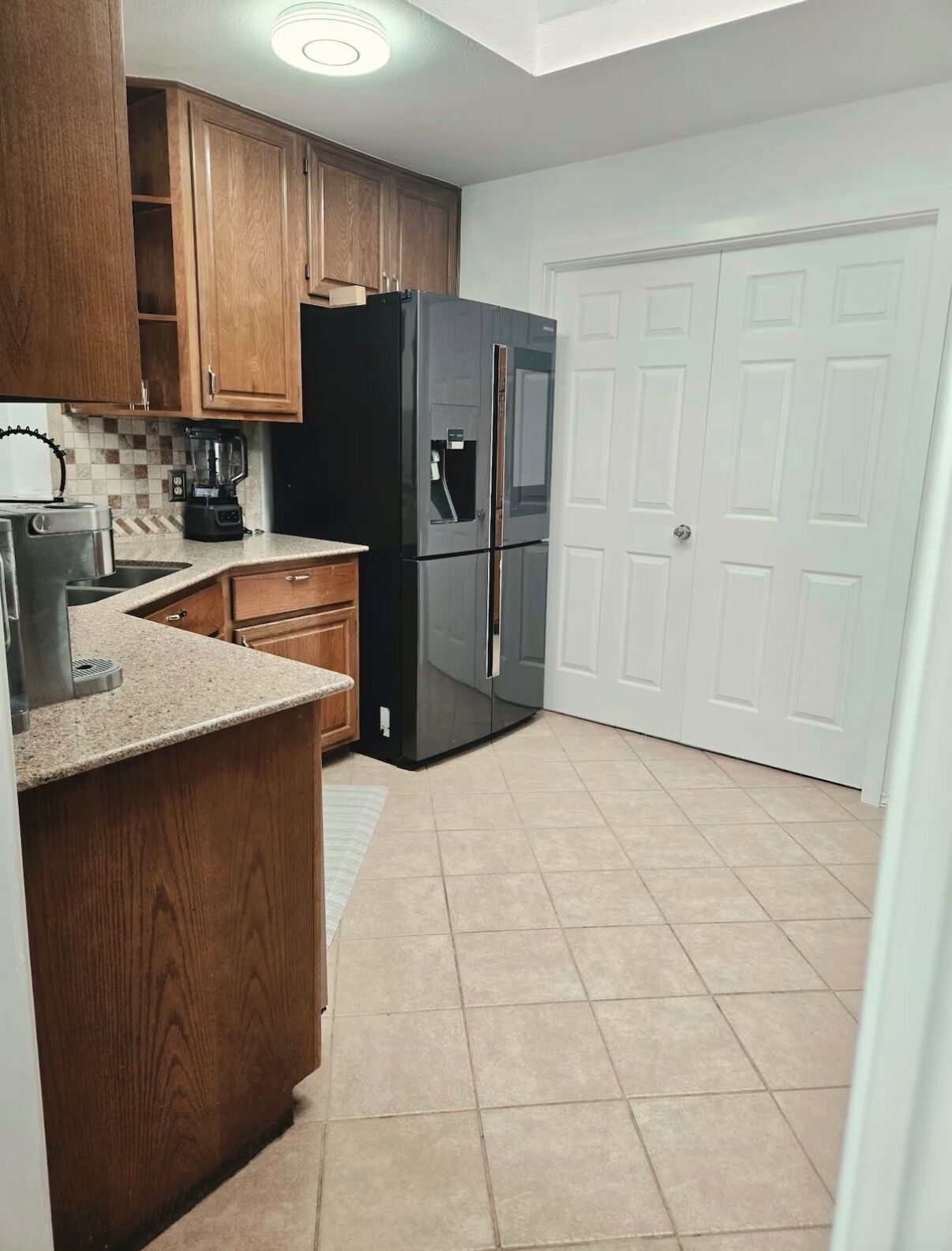 A kitchen with wooden cabinets, a black refrigerator, a coffee maker, and a tiled floor.