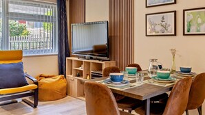A modern living room with a television, dining table, chairs, and artwork on the wall. - 3 Bed in Bridport (oc-94692) (Fernhill)