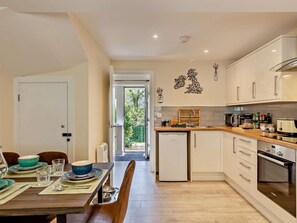 Une cuisine moderne avec des armoires blanches, un four encastré et un coin repas agrémenté d’une table en bois mise pour deux personnes.