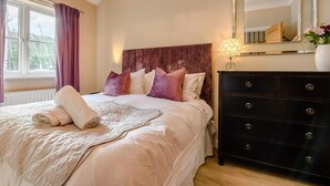 Une chambre à coucher avec un lit, une commode, un miroir et une fenêtre avec des rideaux.