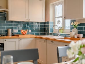 A kitchen with teal backsplash, white cabinets, a wooden countertop, a sink, and a window with flowers. - 3 Bed in Plymouth (oc-45208) (Plymouth)