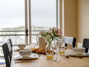 A dining table set with plates, bowls, glasses, and a pitcher of juice, with a view of the city through large windows. - 3 Bed in Plymouth (oc-45208) (Plymouth)