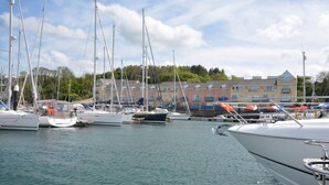 Un port de plaisance où sont amarrés de nombreux voiliers, une surface d’eau calme et une rangée de bâtiments en arrière-plan.
