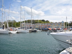 A marina with multiple sailboats docked, a calm water surface, and a row of buildings in the background. - 3 Bed in Plymouth (oc-45208) (Plymouth)