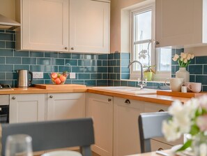 A kitchen with teal backsplash, white cabinets, a wooden countertop, a sink, and a window with flowers. - 3 Bed in Plymouth (oc-45208) (Plymouth)