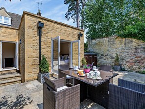 Ein Steinhaus mit einer Terrassenfläche, ausgestattet mit Korbmöbeln, einem Tisch mit Kuchen und Topfpflanzen.
