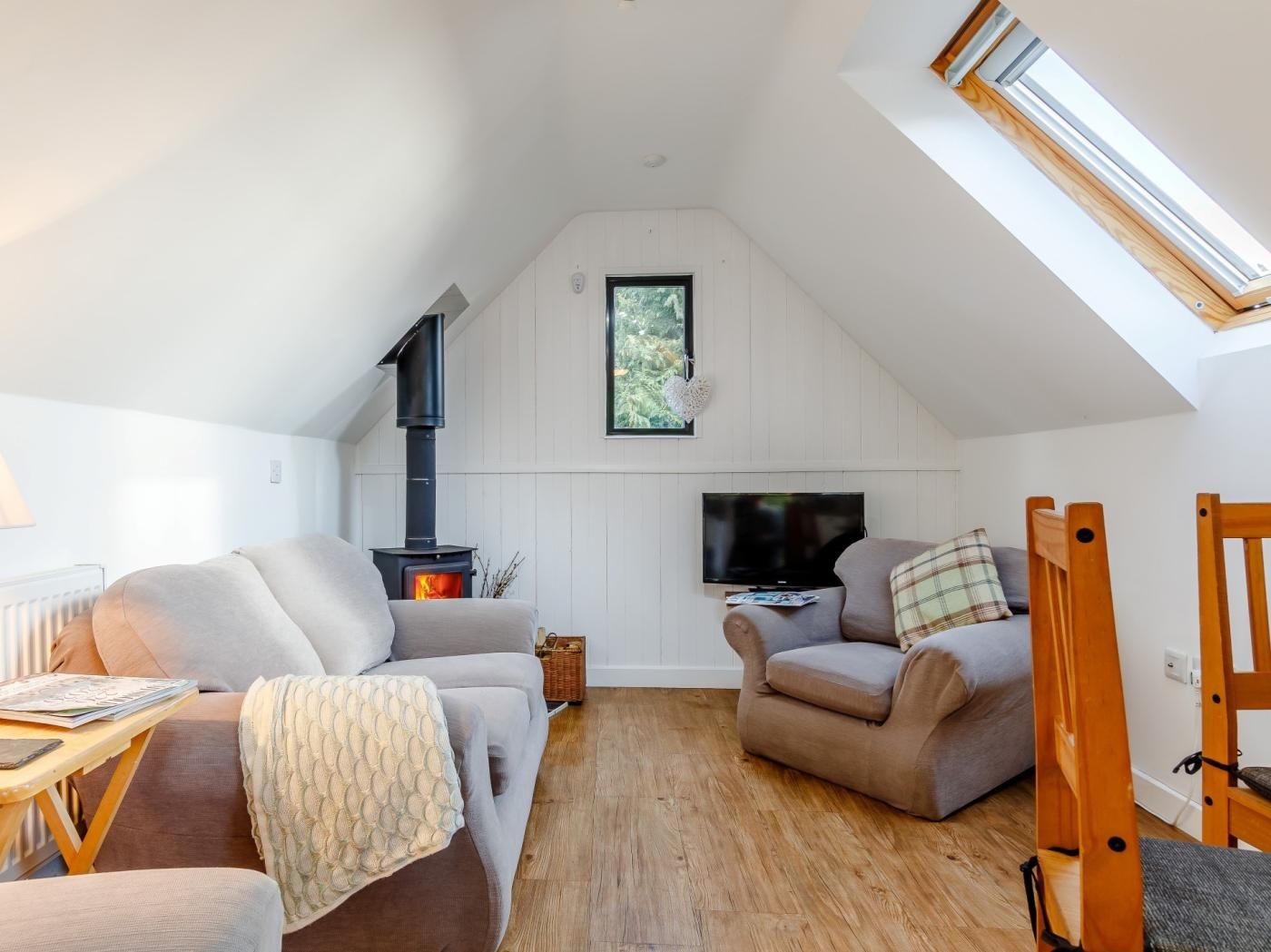 Ein gemütliches Wohnzimmer im Loft-Stil mit eingebautem Kamin, einem Fernseher und einer komfortablen Sitzecke mit hoher Decke und Dachfenster.