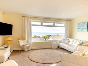 Ein Wohnzimmer mit großem Fenster, Flachbildfernseher, einer Couch, einem Sessel und einem kleinen Tisch mit Getränken.