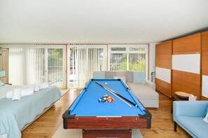 Une table de billard dans une pièce qui comprend un lit, un canapé et de grandes fenêtres offrant une vue sur l’extérieur.