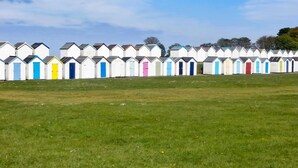 Une rangée de cabanes de plage, avec un champ d’herbe devant.