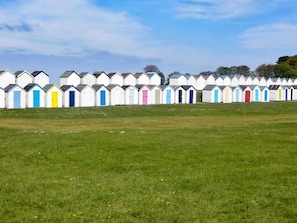 A row of beach huts with a grassy field in front. - 4 Bed in Paignton (oc-56920) (Paignton)