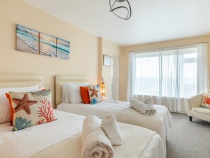 Une chambre d’hôtel avec deux lits, un coin salon et une grande fenêtre avec des rideaux.