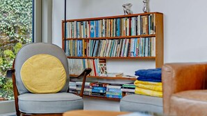Ett modernt vardagsrum med en bokhylla, en grå fåtölj med en gul kudde och en lädersoffa.