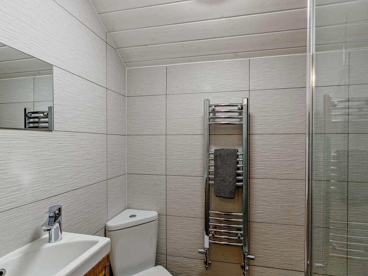 Ein Badezimmer mit weißem Waschbecken, Toilette, Handtuchhalter und einer Duschkabine aus Glas.