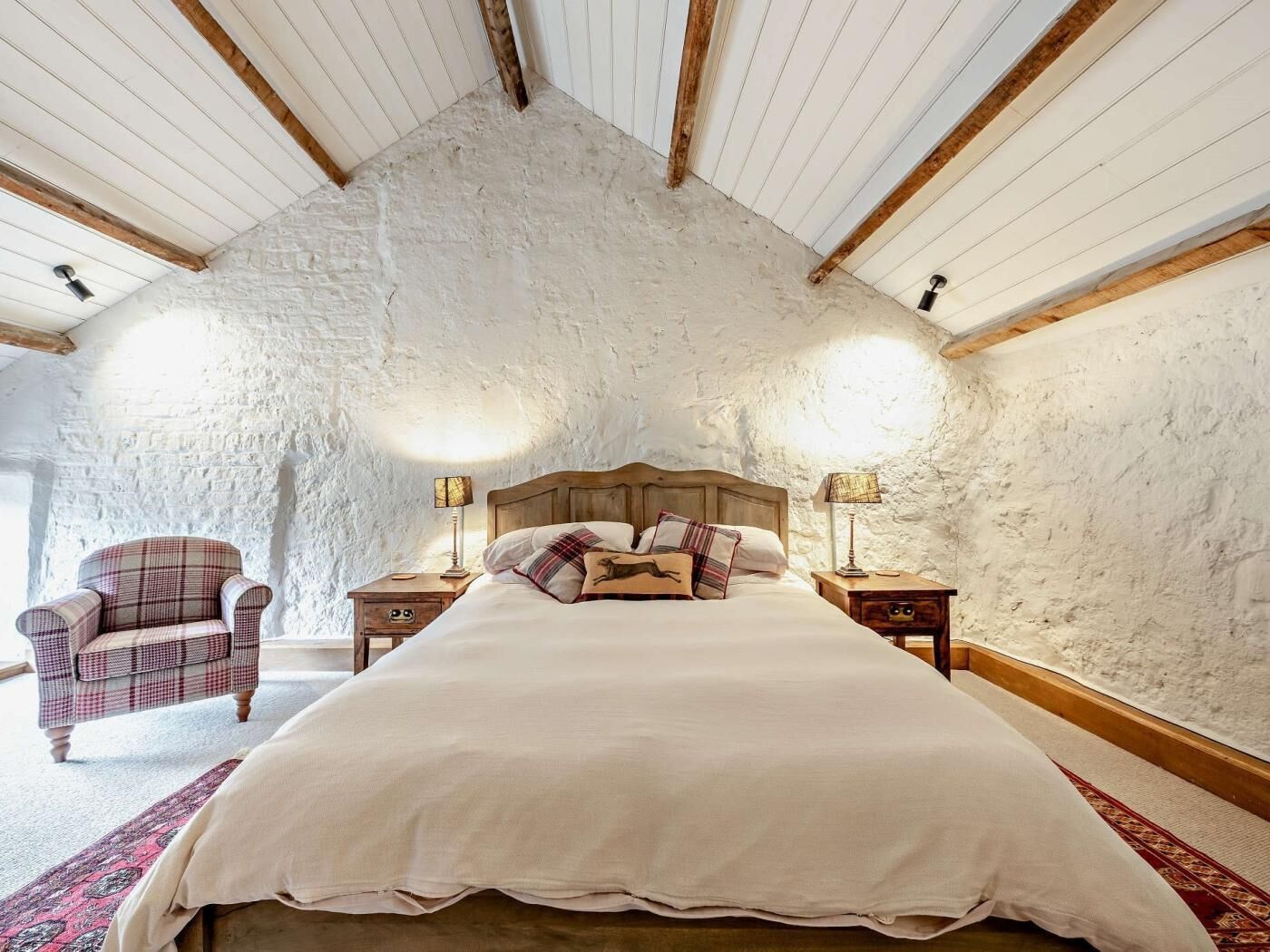 Um quarto com uma cama grande, duas mesas de cabeceira, uma cadeira e uma parede de pedra rústica.