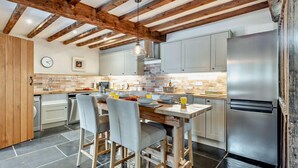 A modern kitchen with exposed wooden beams, a central island with chairs, a stainless steel refrigerator, and a tiled backsplash. - 2 Bed in Exeter (oc-92739) (Longdown)