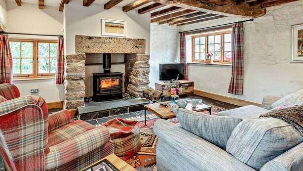 A cozy living room with a stone fireplace, wooden beams, plaid furniture, and a television. - 2 Bed in Exeter (oc-92739) (Longdown)