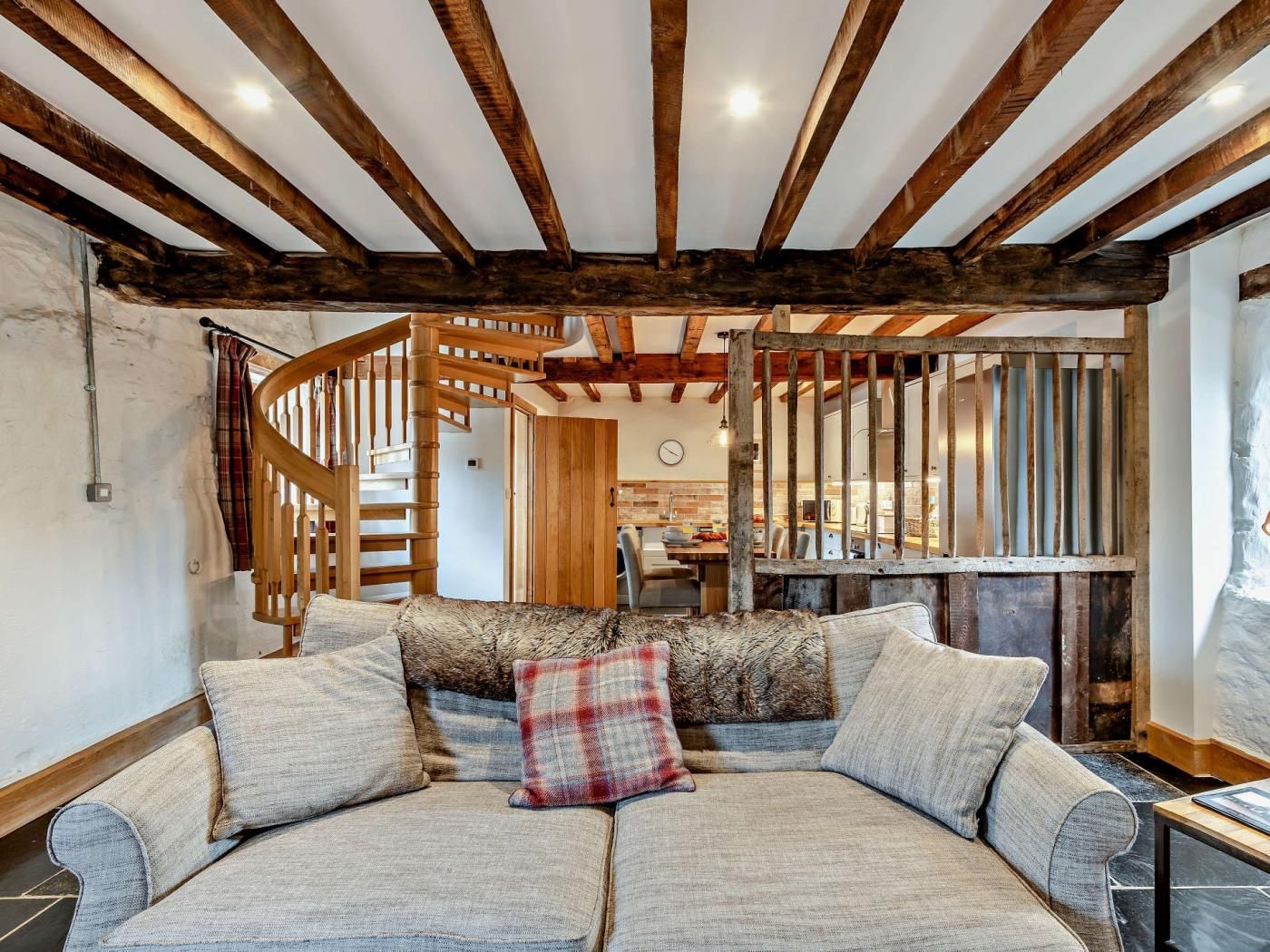 A cozy living room with a wooden staircase, a sofa with cushions, and a view into the kitchen area.